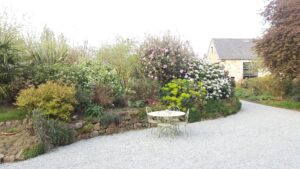 Table de jardin en fer forgé devant un massif fleuri de printemps et le gîte en pierre normande