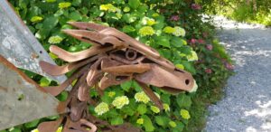 Sculpture de tête de cheval en métal récupéré devant un massif d'hortensias