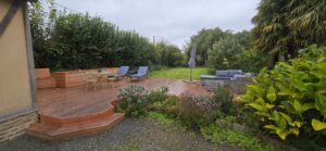Terrasse en bois à plusieurs niveaux bordée de massifs, gîte de La Filuzière en Normandie