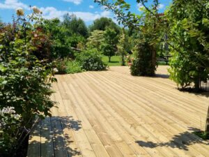 Grande terrasse en bois entourée de rosiers et de massifs, jardin de La Filuzière