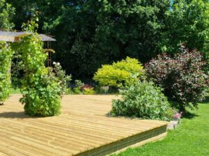 Terrasse en bois et gloriette fleurie ouvrant sur la pelouse du jardin