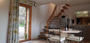 Escalier hélicoïdal du gîte menant à la mezzanine, coin repas et cuisine au premier plan