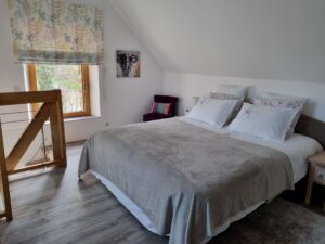 Grand lit de la chambre parentale en mezzanine, éclairé par la lumière du jardin