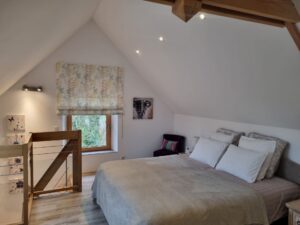 Chambre parentale en mezzanine sous charpente, grand lit et fenêtre sur la campagne