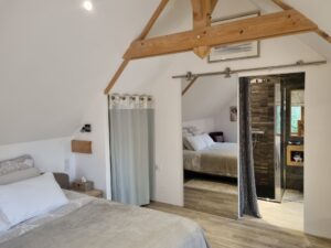 Chambre parentale du gîte avec porte coulissante vitrée et charpente apparente