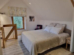 Chambre parentale en mezzanine avec grand lit, chevet et fenêtre sur le jardin