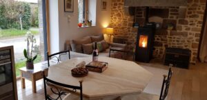 Séjour du gîte : table ronde, canapé et poêle à granulés devant la cheminée en pierre