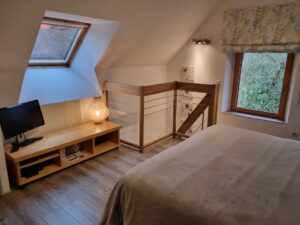 Chambre parentale en mezzanine avec téléviseur, fenêtre de toit et garde-corps en bois