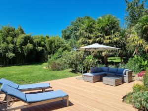Terrasse en bois du gîte avec bains de soleil et salon d'extérieur, ouverte sur le jardin